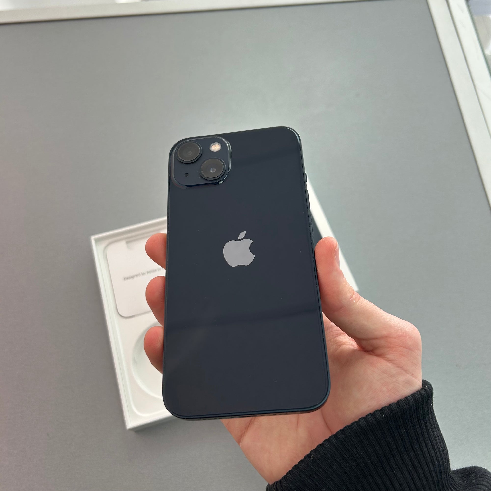 Person holding a black iPhone with Apple logo on a gray surface