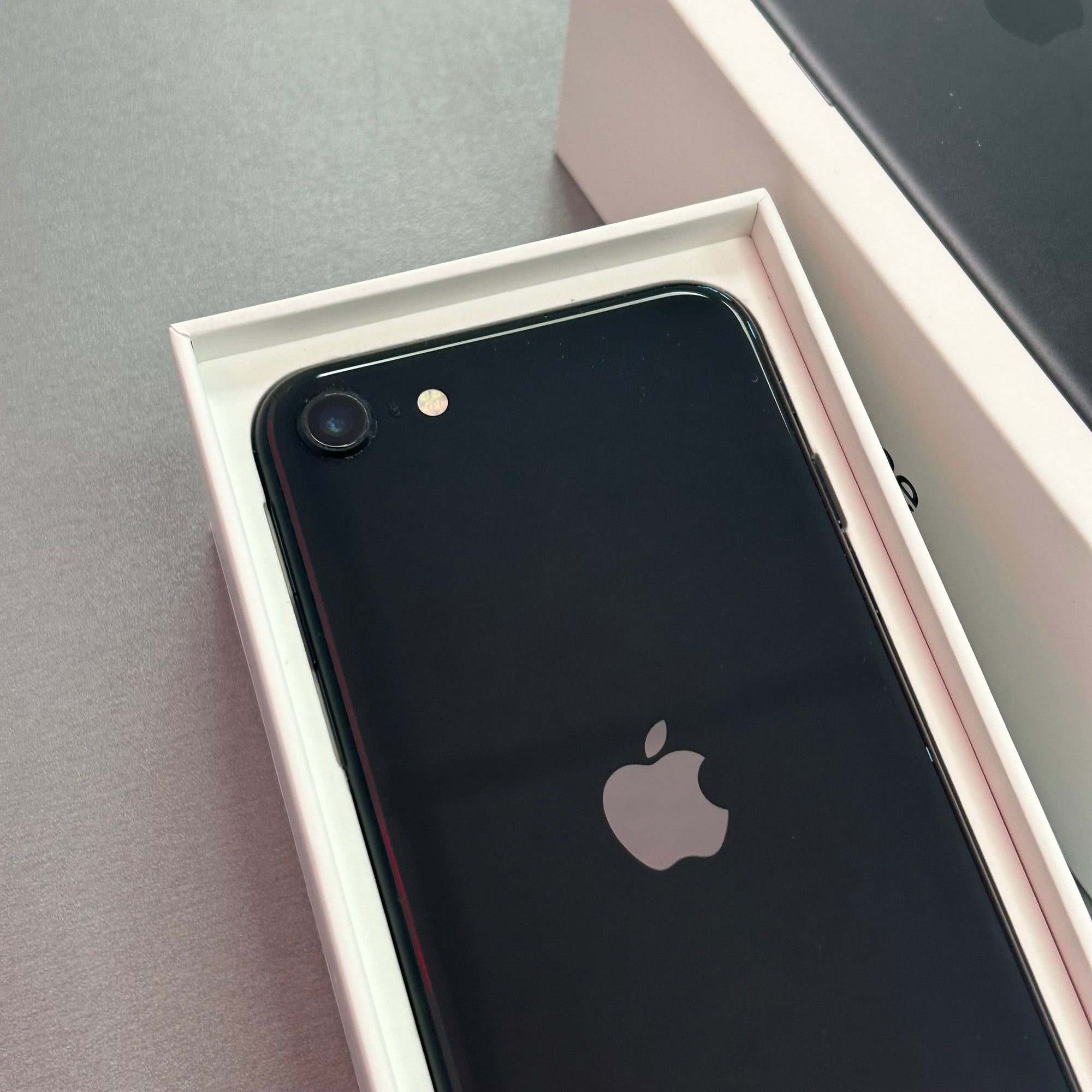 Black smartphone with Apple logo in an open box on a gray surface