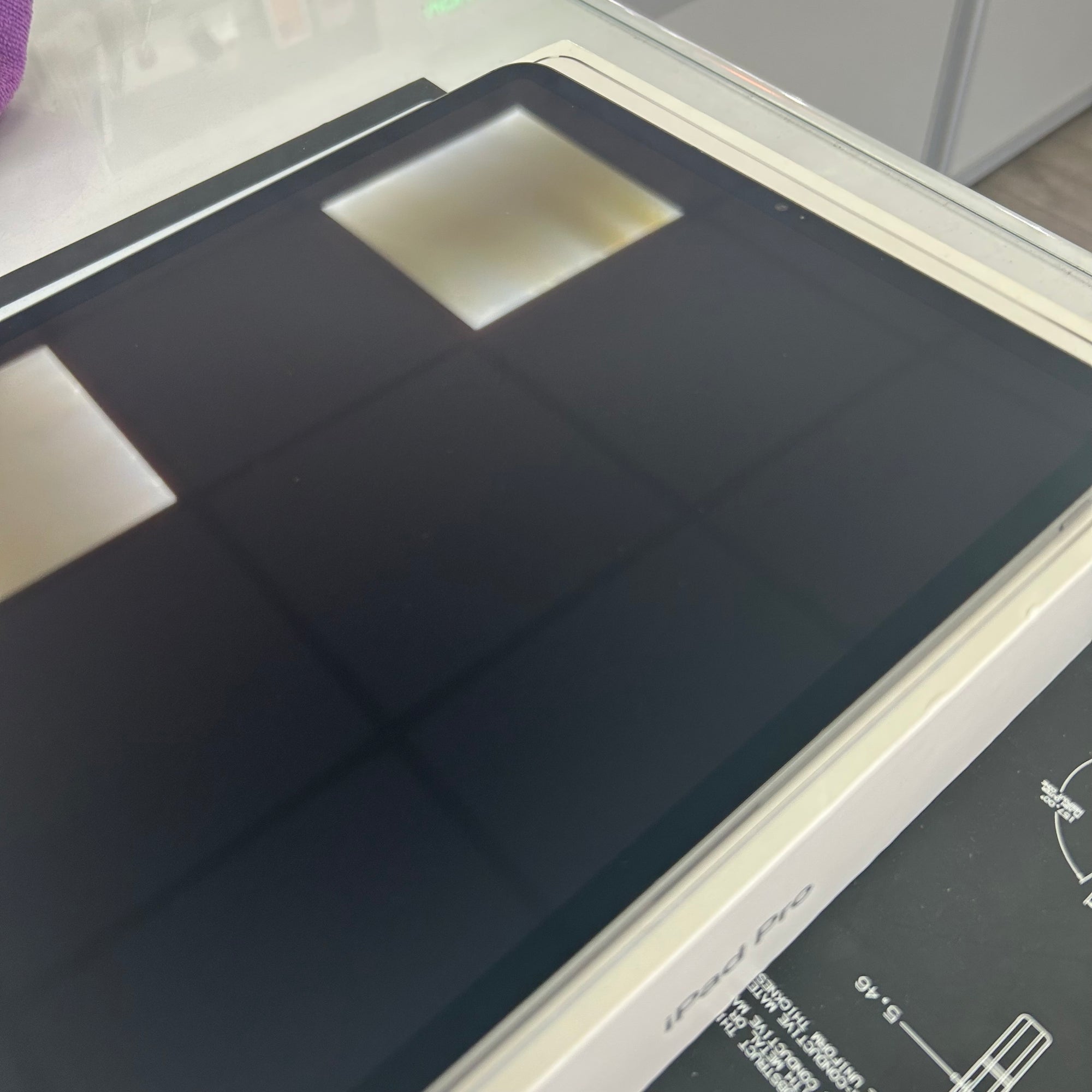 A close-up of a black rectangular panel or mat with a glossy finish, resting on a white surface with part of a printed diagram visible underneath.